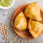 traditional indian food samosa in wooden  plate with mint chutney on a gray concrete background. top view, close up, flat lay.